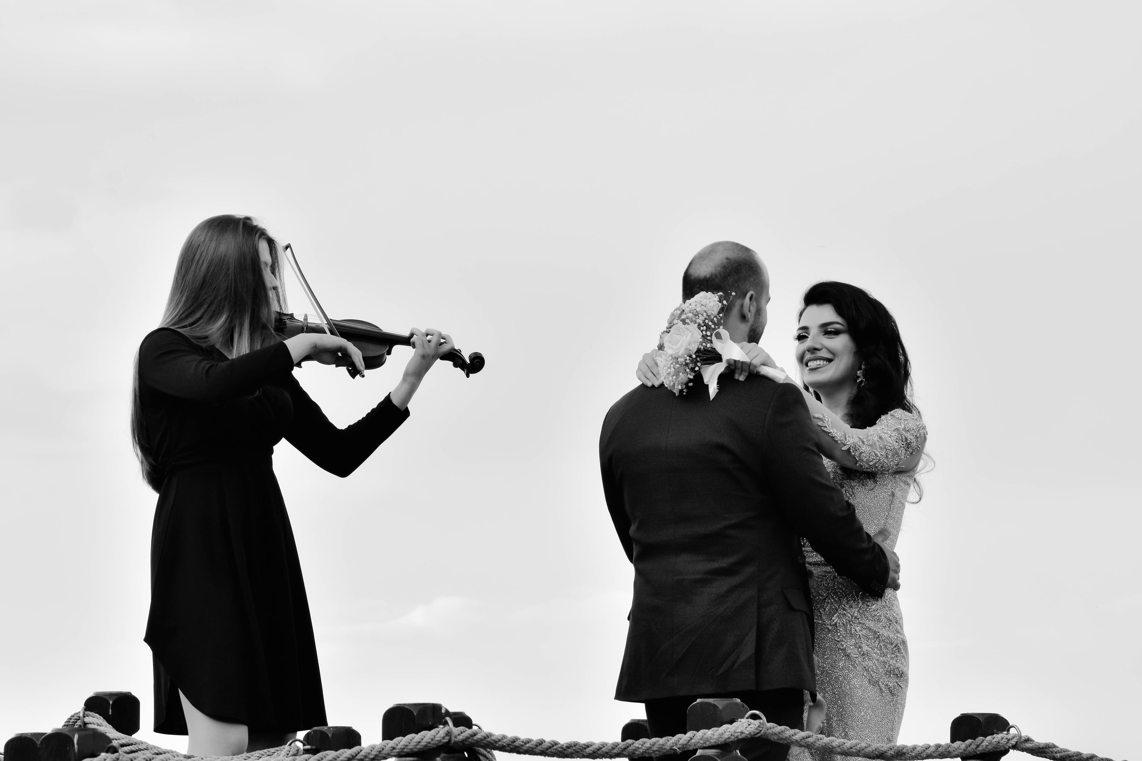 Violinist playing as a bride and groom embrace on a rope-lined deck