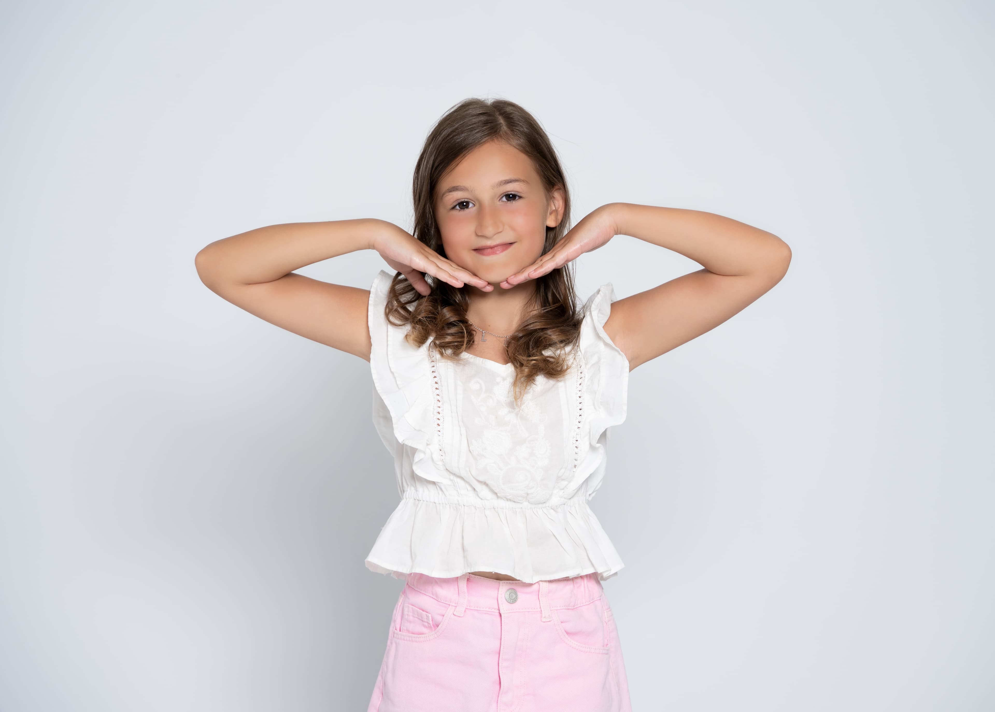 Smiling girl in a white ruffled top resting her chin on her hands in the studio