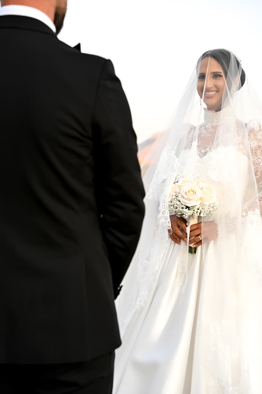 Smiling bride under her veil holding a bouquet of white roses