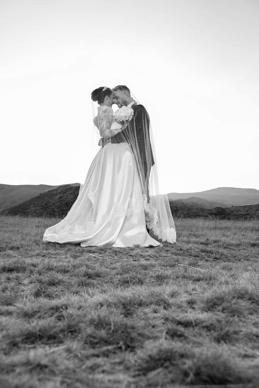 Bride and groom embracing under a veil on a mountain meadow
